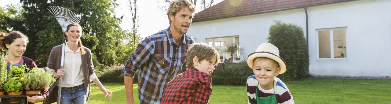 Man pushing two boys in wheelbarrow in front of single family house