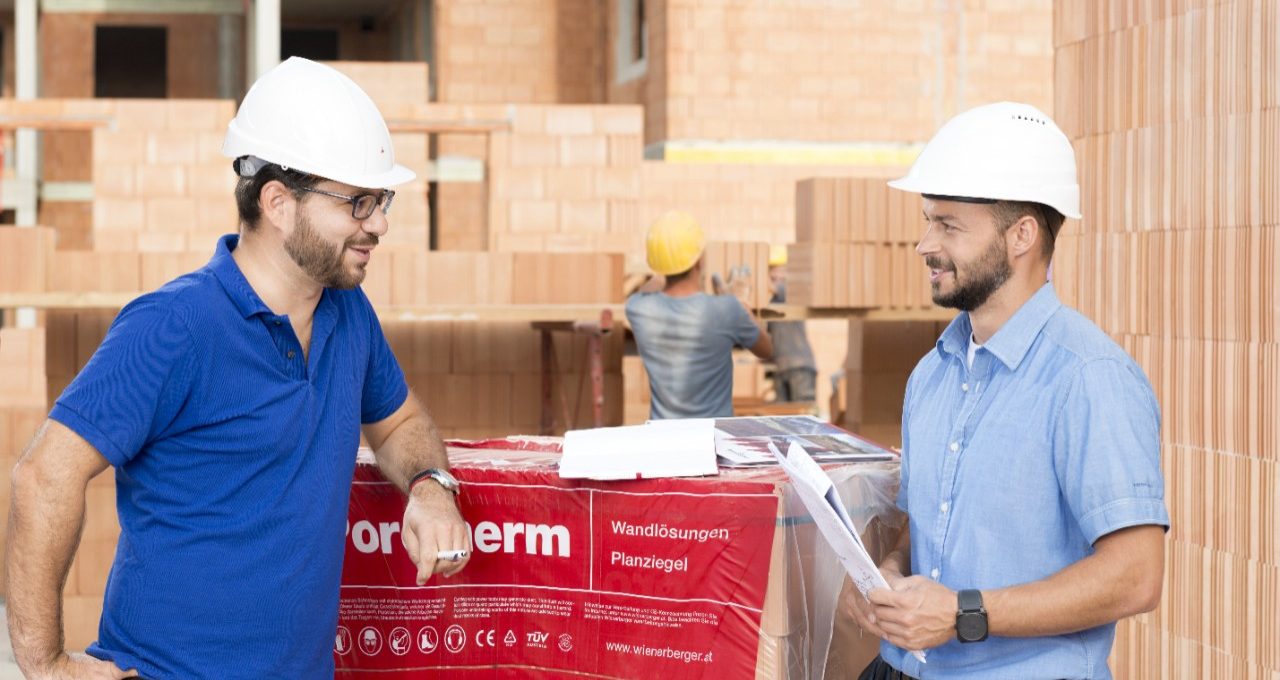 Building professionals talking at construction site next to foil wrapped pallette of brick blocks. > There is another version of this image available without the worker in the background - WB002389