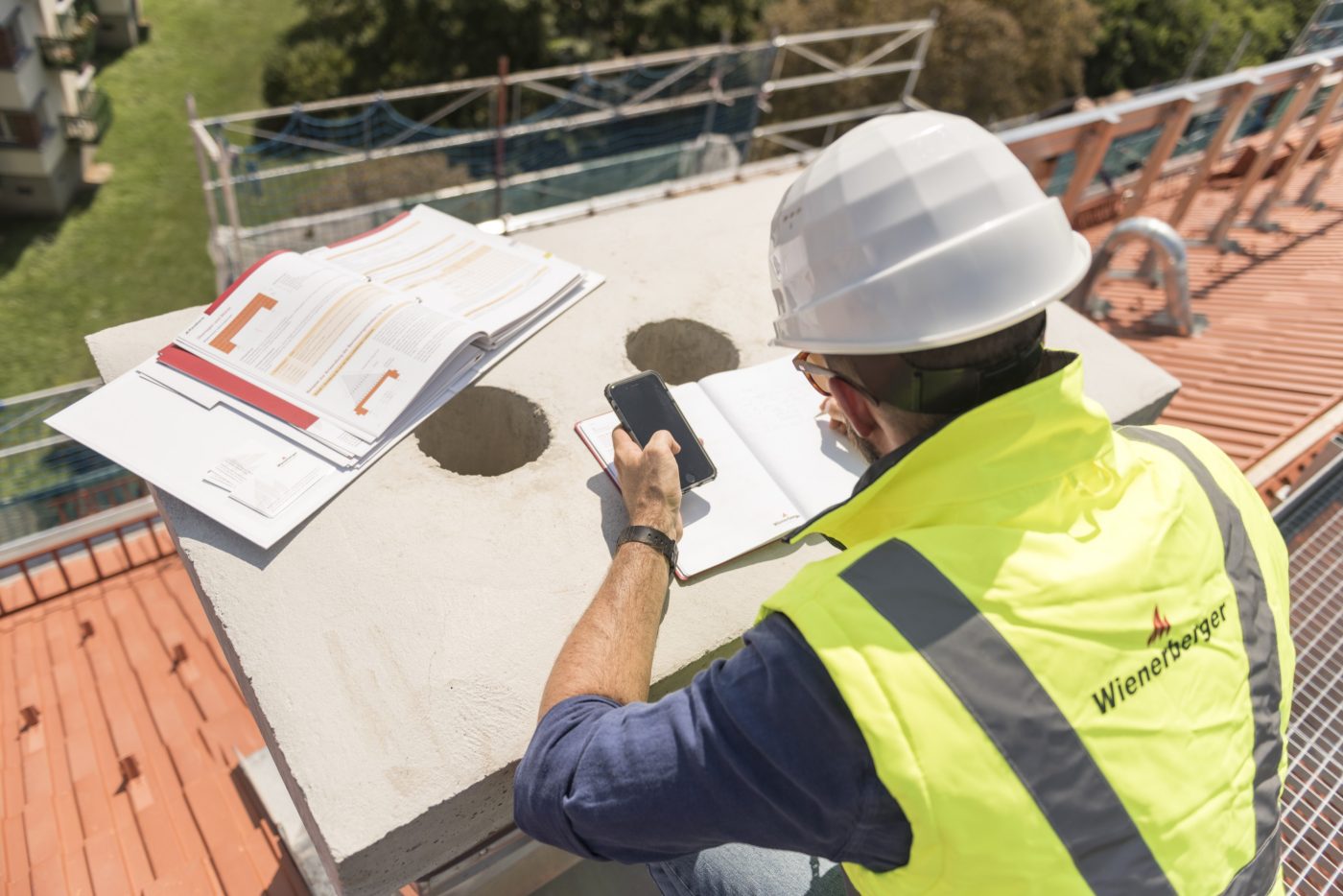 Urban roofer taking notes holding iPhone and writing in an urban location wearing hard hat and safety jacket, Fast Forward Commercial Excellence