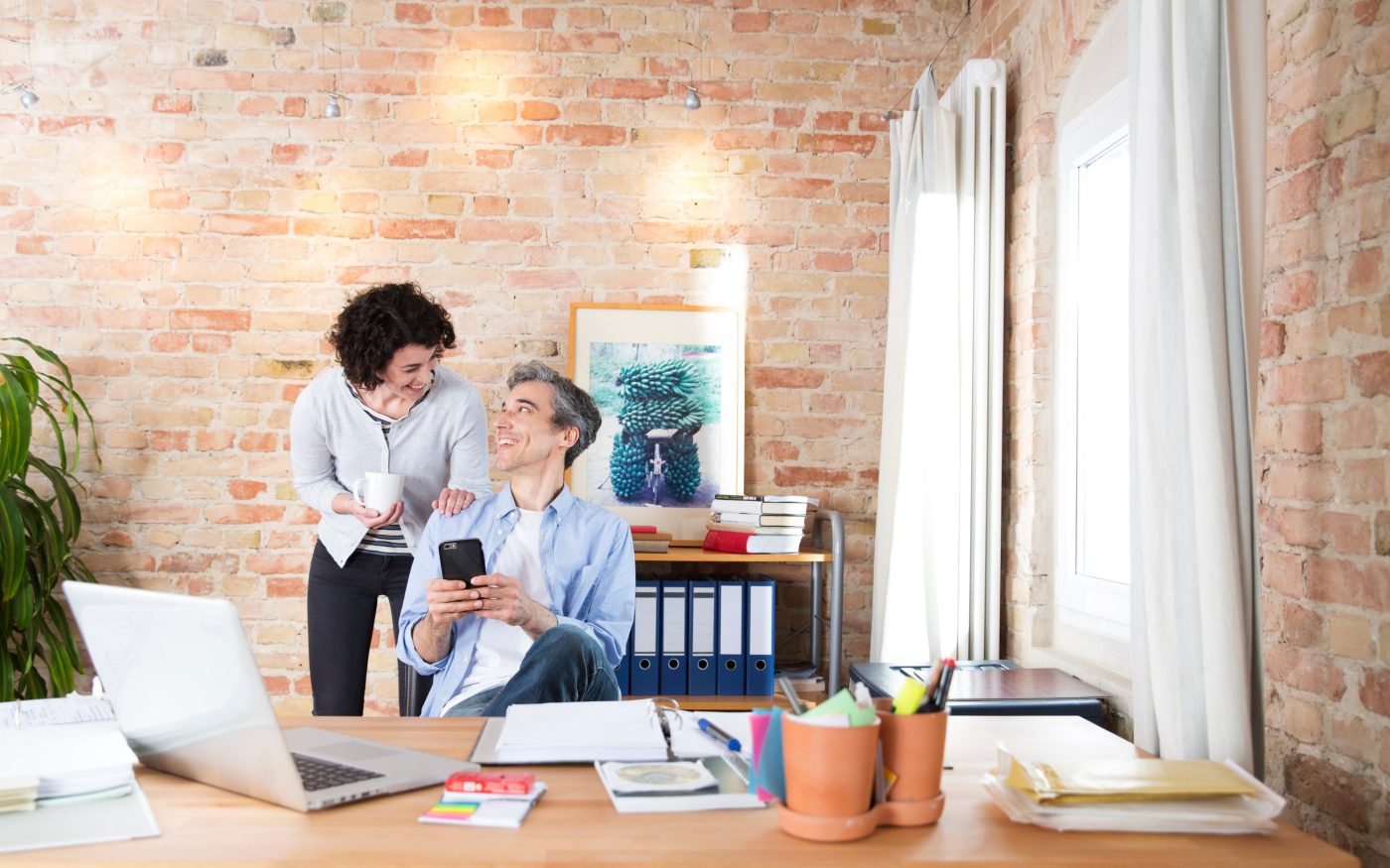 Man with phone in conversatuion with woman in front of brick-lined wall