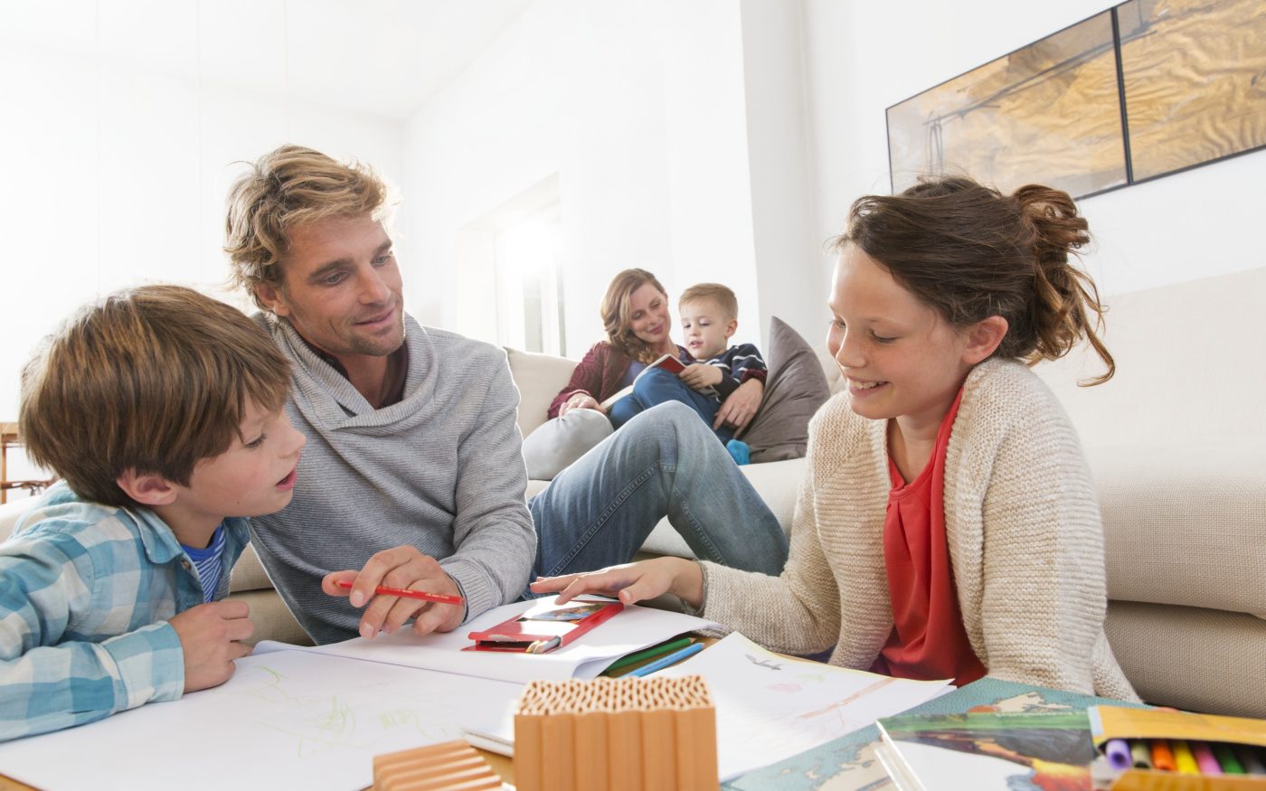 Father with two kids sketching and mother with boy reading a book in living room