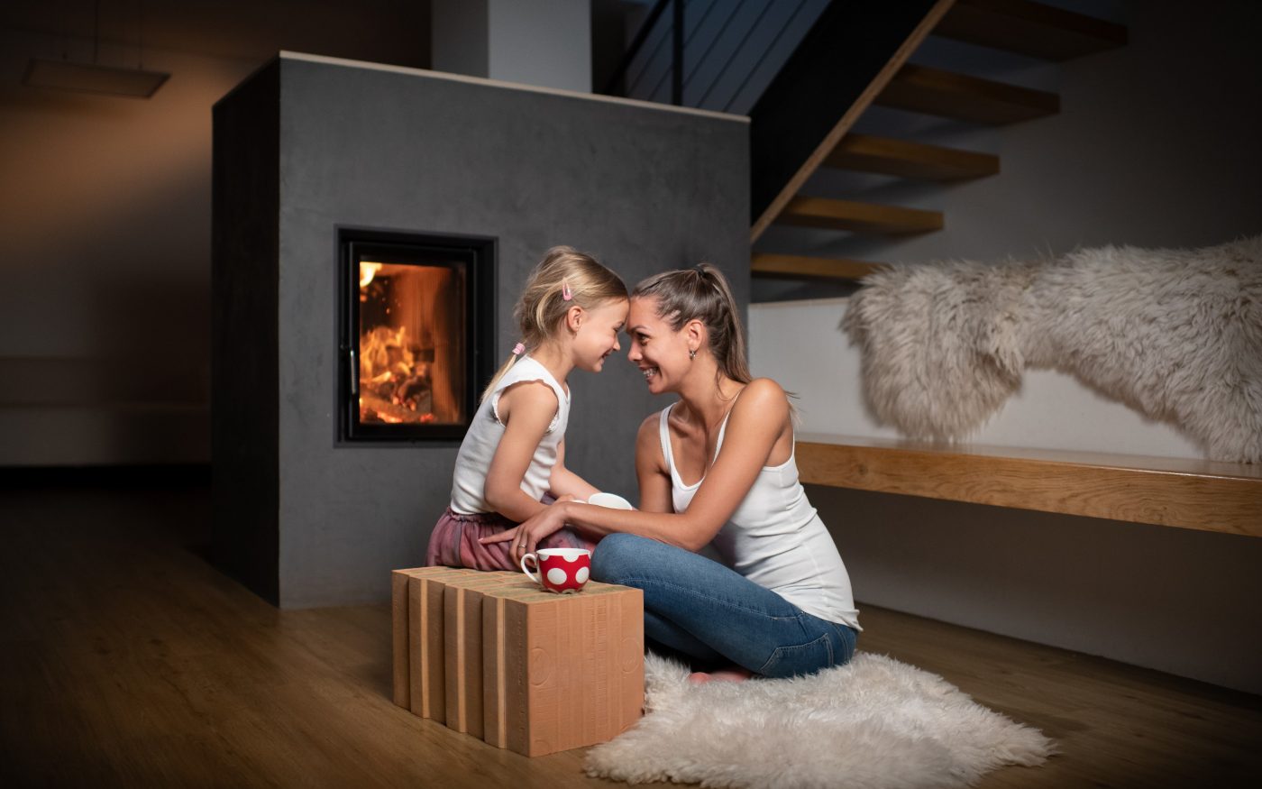 Zena s ditetem sedicim na cihle Porotherm T Profi (vatovka) v obyvaku pred krbem - Lifestyle image