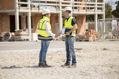 Manager and builder shaking hands on construction site in front of building shell